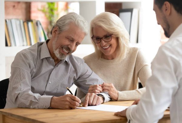 Happy older family couple clients make sale purchase deal sign insurance contract meeting estate agent lawyer bank manager, satisfied senior customers make business financial deal buy house take loan